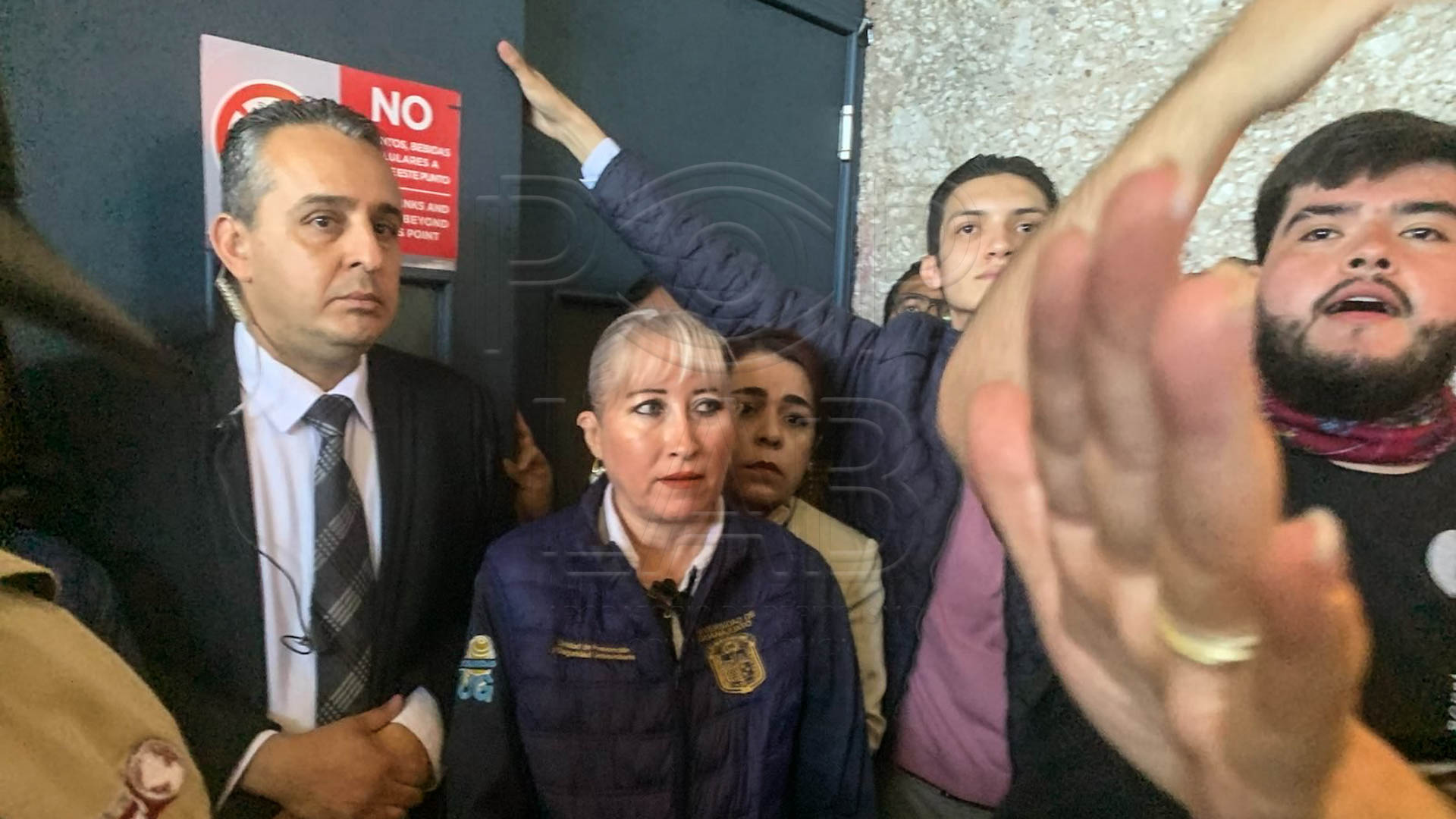 Dolores Gallegos, secretaria particular de Guerrero Agripino de saco café, detrás de elementos de seguridad para impedir el acceso de estudiantes